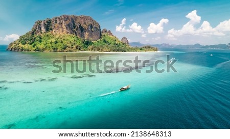 Tropical turquoise water with a Thai longtail boat motoring past a coral reef and Ko Poda Island in the Andaman sea of Krabi Thailand