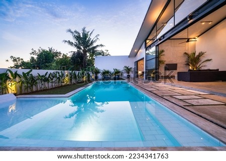 Tropical villa view with garden, swimming pool and open living room at sunset.
