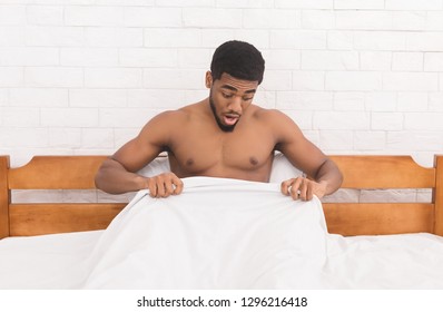 Trouble with erection. Young african-american man in bed having problems with potency, looking at his penis under blanket, copy space