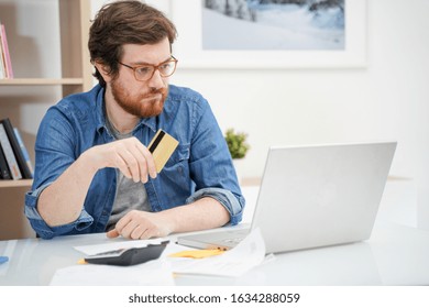 Troubled bearded guy holding credit card and using laptop - Shutterstock ID 1634288059