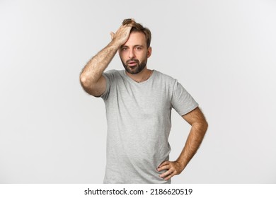 Troubled bearded man in gray t-shirt, slap forehead and sighing bothered by problem, standing over white background distressed - Shutterstock ID 2186620519