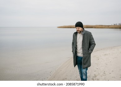 Troubled Depressed Man Walking Along A Deserted Beach On A Cold Winter Day Looking Down At The Sand With A Serious Thoughtful Expression