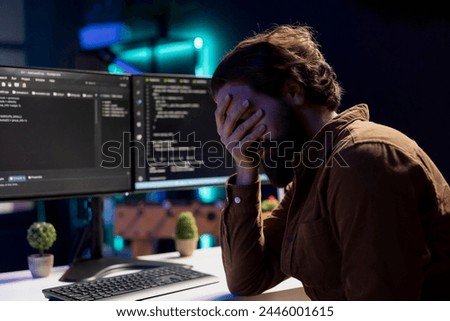 Troubled man facepalming himself while doing software quality assurance, finding major errors in source code. Depressed developer upset after inspecting coding on desktop PC and seeing many issues