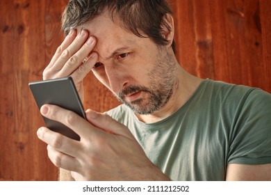 Troubled Man Receiving Unpleasant Sms Message Notification On Mobile Smart Phone, Reading Text Message In Disbelief