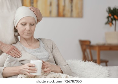 Troubled Patient With Cancer Tumor Holding A Cup Of Tea While Being Comforted By A Family Member