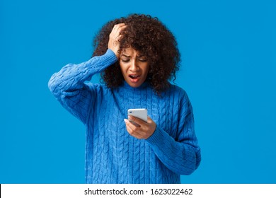 Troubled and upset, worried young woman feeling panic and anxiety, grab head, reading shocking news on smartphone, react to troublesome message, alarmed standing blue background - Powered by Shutterstock