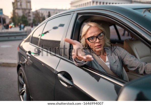 Troubles on the road. Portrait of angry business\
woman gesturing with hands and arguing with somebody while driving\
a car. Driving. Emotional\
person