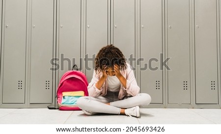 Troubles at school. Lonely sad african-american schoolgirl crying at school hall. Social exclusion problem. Bullying at school concept. Racism problem.Puberty difficult age