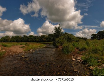 Trout stream among fields with dramatic clouds above