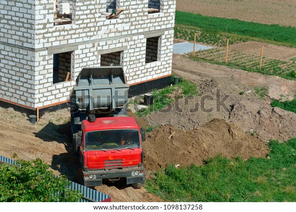 the truck and building of the house from a\
white brick, the dump truck brought sand on building, the dump\
truck near the house under\
construction