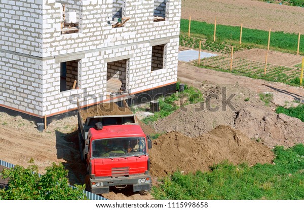 a truck and a building made of white brick,\
the dumper brought sand to the construction site, a dump truck near\
the house under construction