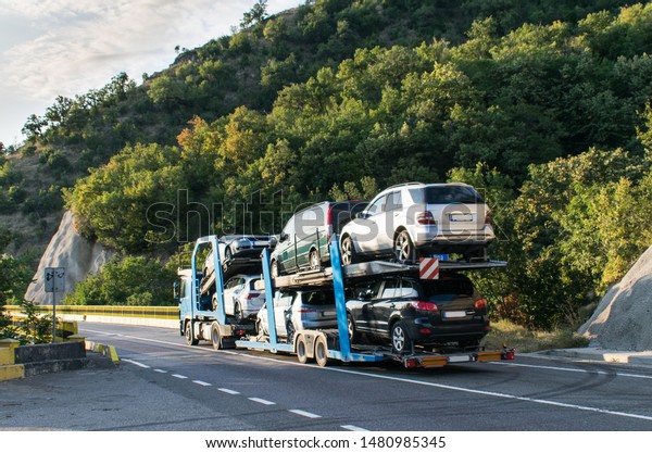 Truck carrying cars. Car carrier semi-truck.\
injured cars transported on the car platform on a mountain road in\
a summer day. Hauling\
cars.