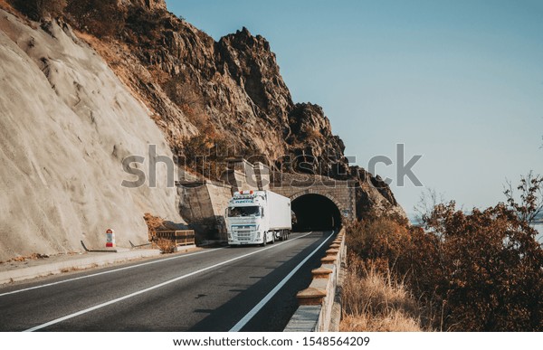 Truck carrying goods on a mountain road, at the exit\
of a tunnel. A beautiful autumn day in traffic. This is a VOLVO\
truck.  The vehicle is white. AZEM.  Romania, Orsova,  October 29,\
2019