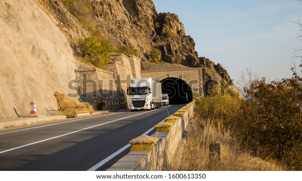 Truck carrying goods on a mountain road, at the exit\
of a tunnel. Beautiful autumn day in traffic. This is a DAF truck.\
The vehicle is white. Auto tranport. Romania, Orsova, November 9,\
2019