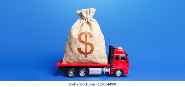 The Truck Is Carrying A Huge Dollar Money Bag. Great Investment. Attracting Large Funds To The Economy For Subsidies, Support And Cheap Soft Loans For Businesses. Anti-crisis Measures Of Government.