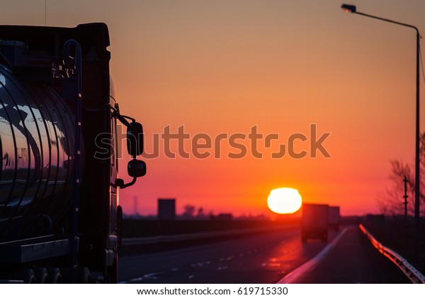 Truck cars on a highway at sunrise with\
beautiful sun in\
background