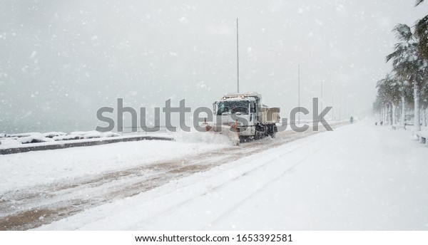 Truck cleaning  winter road covered with snow at the sea\
side 