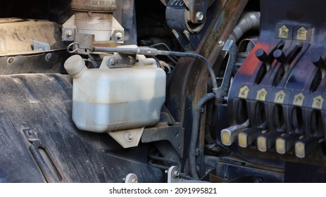 Truck Coolant Tank. White Plastic Tank With Coolant On The Side Radiator System Has A Lever System On The Engine Parts Background With Copy Space. Close-up And Focus On The Subject