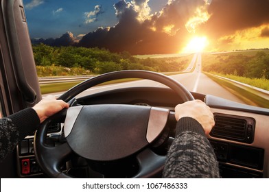 Truck dashboard with driver's hand on the steering wheel on the countryside road in motion against night sky with sunset