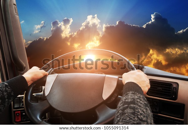Truck dashboard with driver\'s hand on the\
steering wheel against night sky with\
sunset