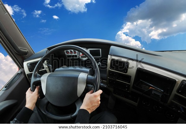 Truck dashboard with driver\'s hand on the\
steering wheel against a blue sky with\
clouds