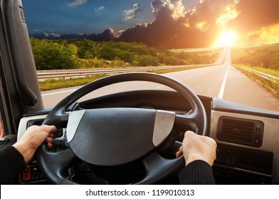 Truck Dashboard With Driver's Hands On The Steering Wheel On The Countryside Road Against Night Sky With Sunset