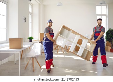 Truck delivery service workers in workwear uniforms removing furniture from house or apartment. Two happy young men from moving company carrying bookshelf together
