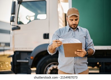 Truck Driver Checking Shipment List While Standing On Parking Lot Of Distribution Warehouse. 