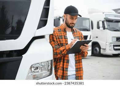 Truck driver checking shipment list while standing on parking lot of distribution warehouse. - Powered by Shutterstock