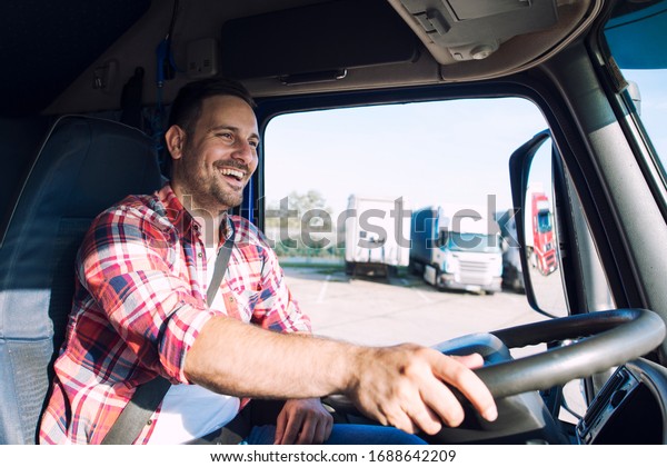 Truck driver job. Middle aged trucker driving\
truck. Professional middle aged truck driver in casual clothes\
driving truck vehicle and delivering cargo to destination.\
Transportation service.