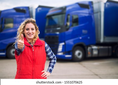 Truck Driver Occupation. Woman Commercial Vehicle Driver In Casual Clothes Holding Thumbs Up In Front Of Truck Vehicles. Transportation Service.