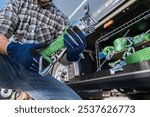 Truck driver is preparing to fasten cargo using ratchet straps from a storage compartment on a vehicle under bright sunlight.