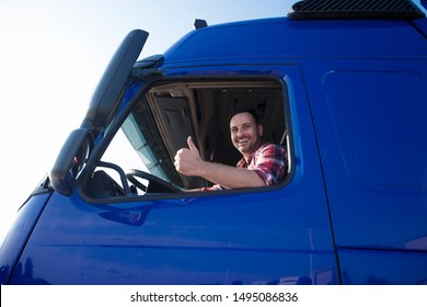 Truck Driver Showing Thumbs Up Through Cabin Window. Positive Smiling Trucker Ready For A New Ride. Transportation Services.