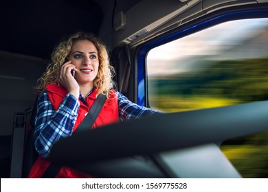 Truck Driver Talking On The Phone While Driving. Woman Trucker Holding Cellphone And Driving Commercial Vehicle On Highway.