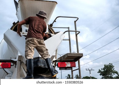 Truck Driver Washing The Cement Mixer Truck After Finish Pouring Cement. Man Standing On The Cement Mixer Truck. Heavy Equipment Machinery For Heavy Industry Concept.