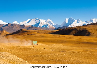 A truck drives through the barren landscape of the mountainous border between Tibet and Nepal as snowcapped himalayan mountain peaks poke through in the distance - Powered by Shutterstock