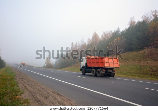 Truck is driving along the road in the morning in a\
thick fog
