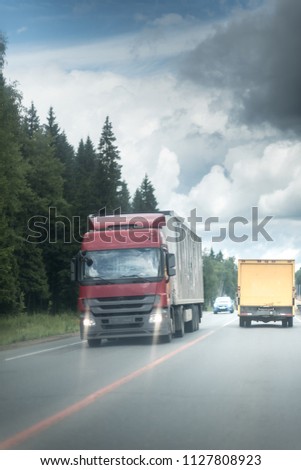 Truck driving on the asphalt road in rural landscape with dark clouds