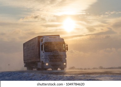 The truck is driving on a snow-covered road at sunset. Snowstorm.