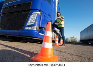 Truck Driving School. Shot Of Bearded Man Learning How To Drive Truck At Driving Schools. Truck Driver Candidate Training For Driving License. Standing By The Traffic Cone In Reflective Vest.