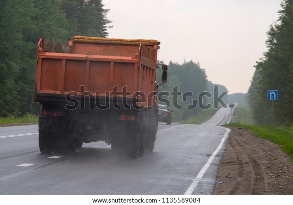 Truck dump with a load of soil in the body rides\
at high speed on the\
highway