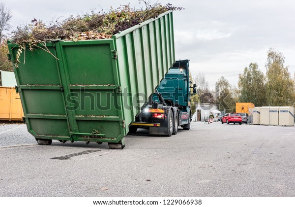 Truck loading container with waste green at\
recycling center to transport it\
away