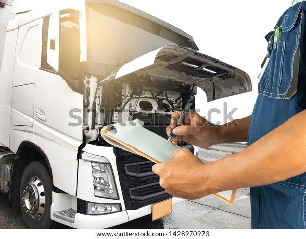 Truck\
maintenance and repairing. professional auto technician holding\
clipboard is inspecting the engine of semi\
truck.