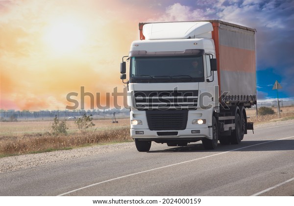 Truck moves on a country road at dawn against the\
backdrop of a cloudy sky