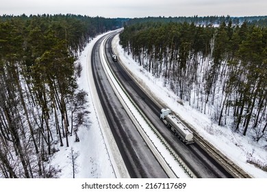 Truck On The Higthway. Gasoline Tanker Driving By Road Seen From The Air. Top View Landscape. Shooting From A Drone. Cargo Delivery In Winter. Aerial View Of Snow Covered Road In Winter Forest 