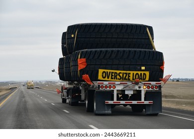 a truck with an oversize load sign carrying gigantic tires with red flags while driving down the highway