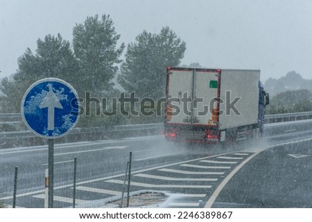 Truck with refrigerated semi-trailer driving on the highway on a day of adverse weather due to snowfall.