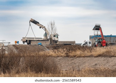 A truck with a telescopic crane unloads building materials at a construction site. - Powered by Shutterstock