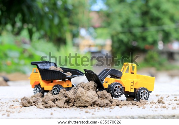 Truck toy car with sand and soil\
on the concrete floor with blur boken green environment \
construction equipment at work ,construction concept, selective\
focus