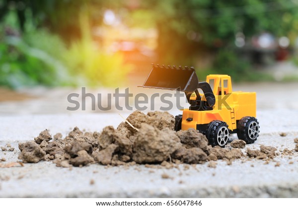 Truck toy car with sand and
soil on the concrete floor with blur boken green environment 
construction equipment at work ,construction concept, selective
focus.